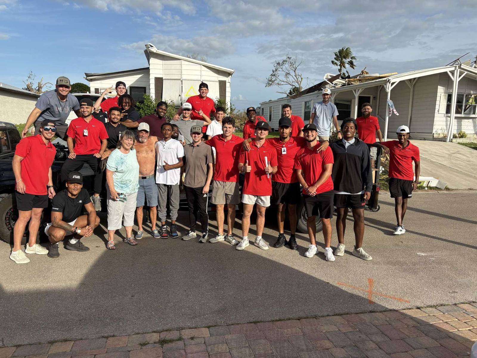 More than twenty HELP volunteers and partner crew members gathered with two residents in front of a storm-damaged mobile home.