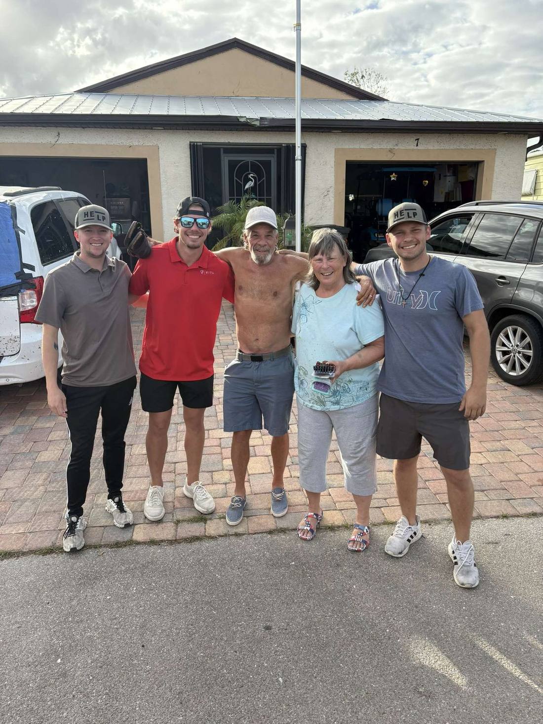 Three HELP volunteers standing arm-in-arm with a homeowner couple outside their storm-damaged house.